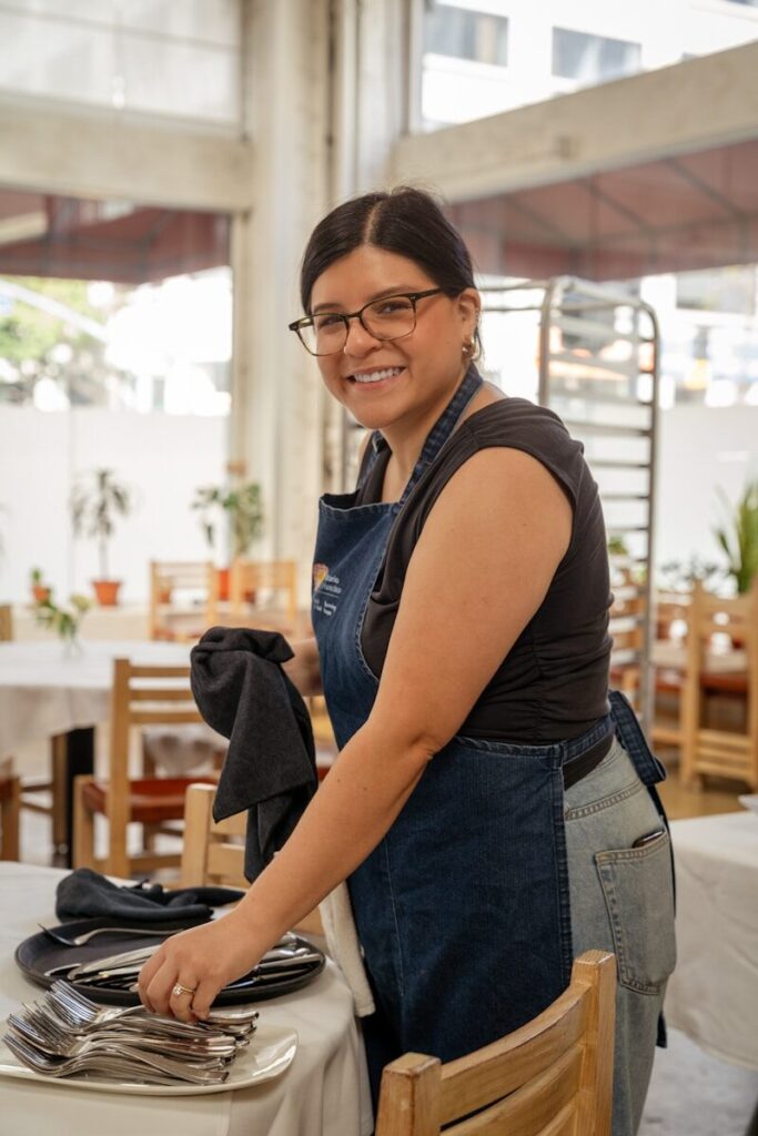 A woman in an apron setting a table with silverware.